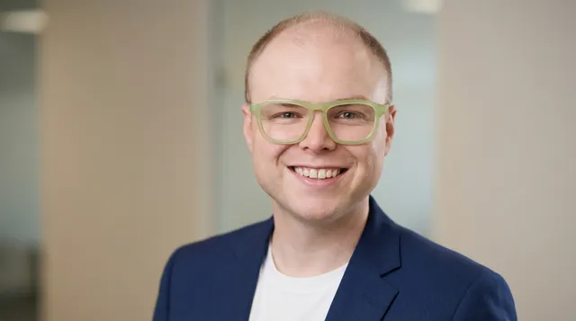Augustus Willman, smiling, in a navy blazer and green glasses