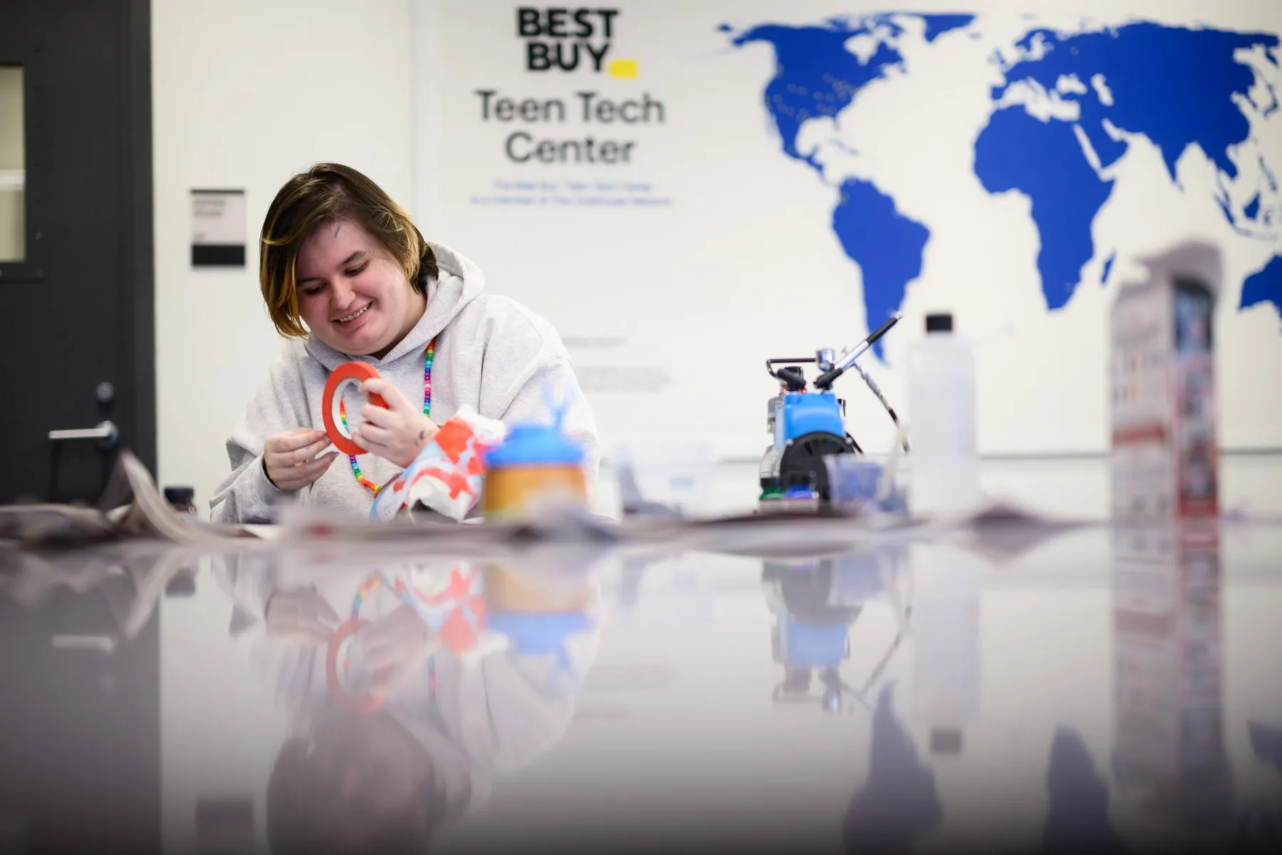 Hypnos smiling while preparing red masking tape for a cleat design inside a Best Buy Teen Tech Center